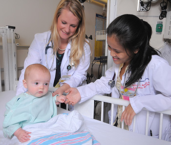Two female residents examining a baby wearing a tiny hospital gown
