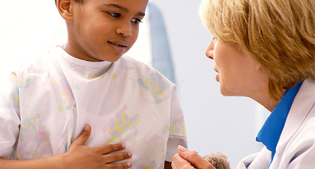 a young child in a hospital gown touching his stomach in pain, and a doctor leaning down talking to him in a comforting way